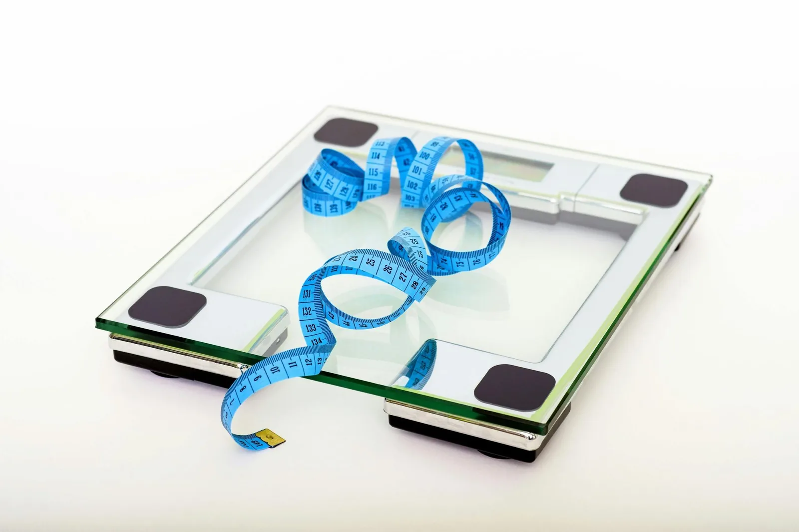 Bathroom scale with a blue measuring tape coiled on the glass surface.